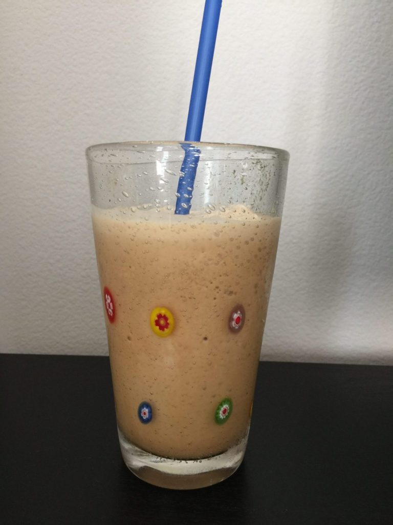 A glass of chilled smoothie with a blue straw, blended with ice and espresso.