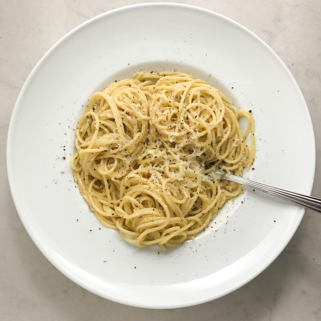 A plate of spaghetti with cacio, parmesan cheese, and parsley.
