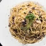 A plate of spaghetti with tuna and black olives.