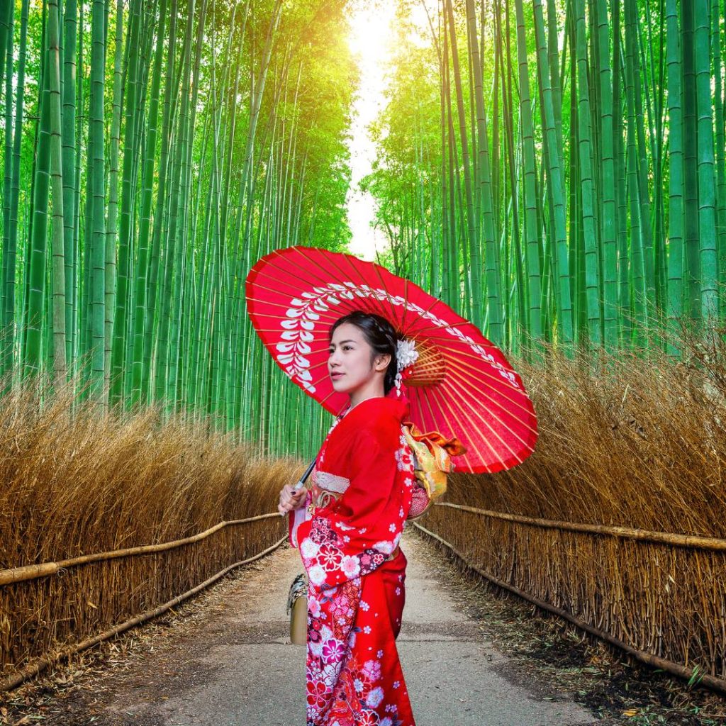 A woman in a red kimono is standing in a bamboo forest in Kyoto.