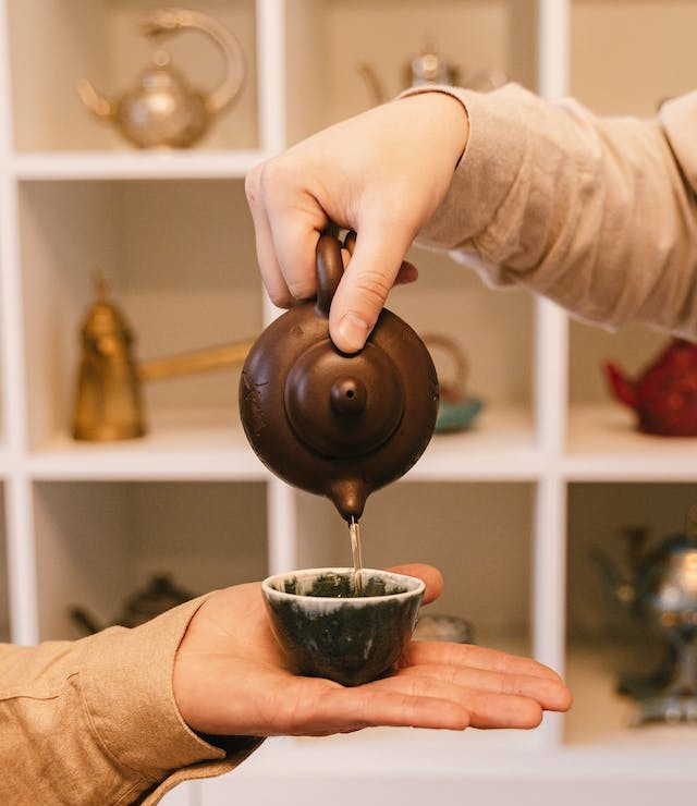 a hand pouring tea from a back handle tea pot