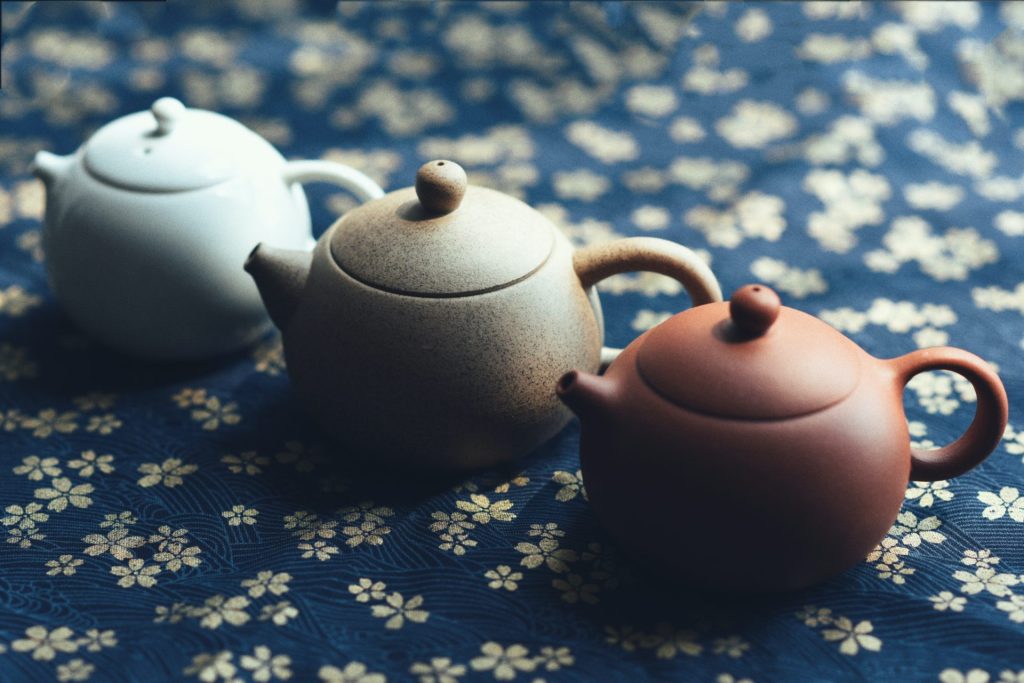 Three Japanese ceramic teapots are lined up on a blue cloth.