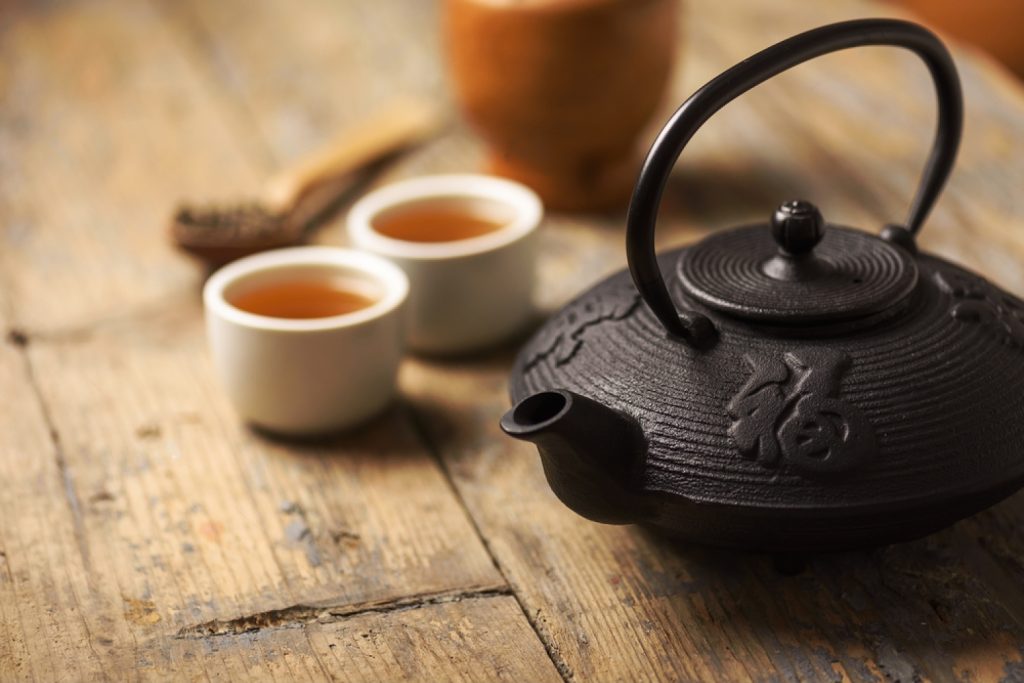 A Japanese cast iron tea pot displayed with two cups of tea on a wooden table.