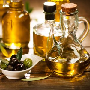 Bottles of olive oil sit on a table with a bowl of olives