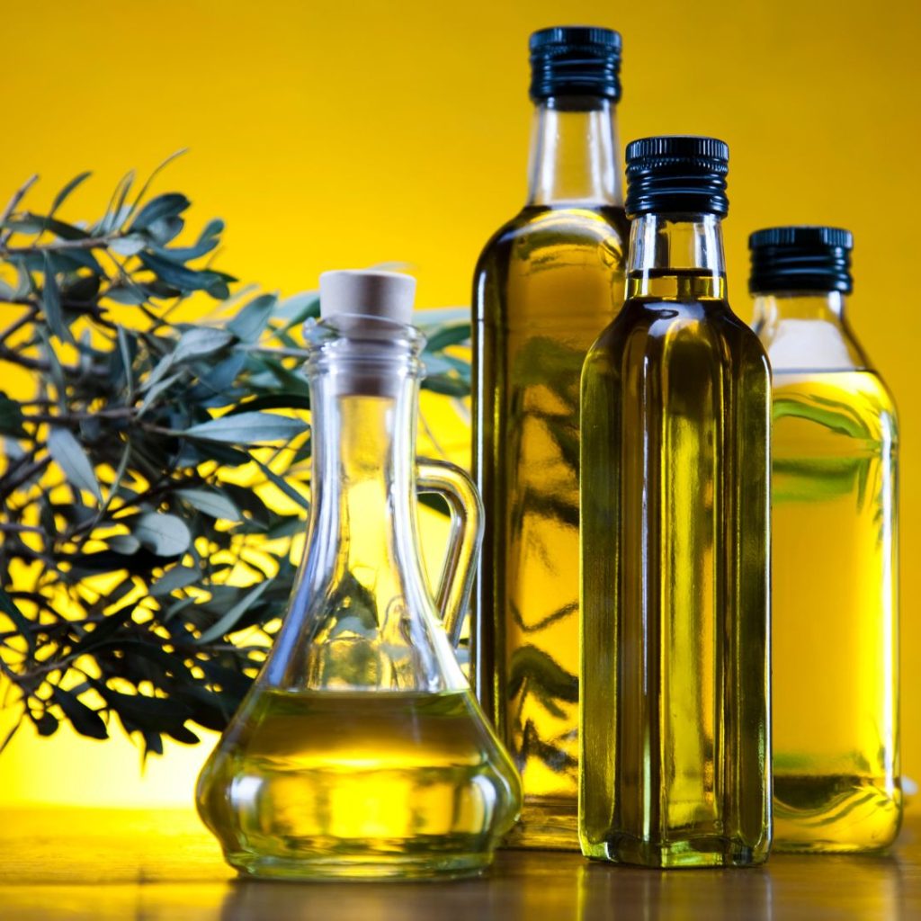 Four bottles of olive oil on a yellow background.
