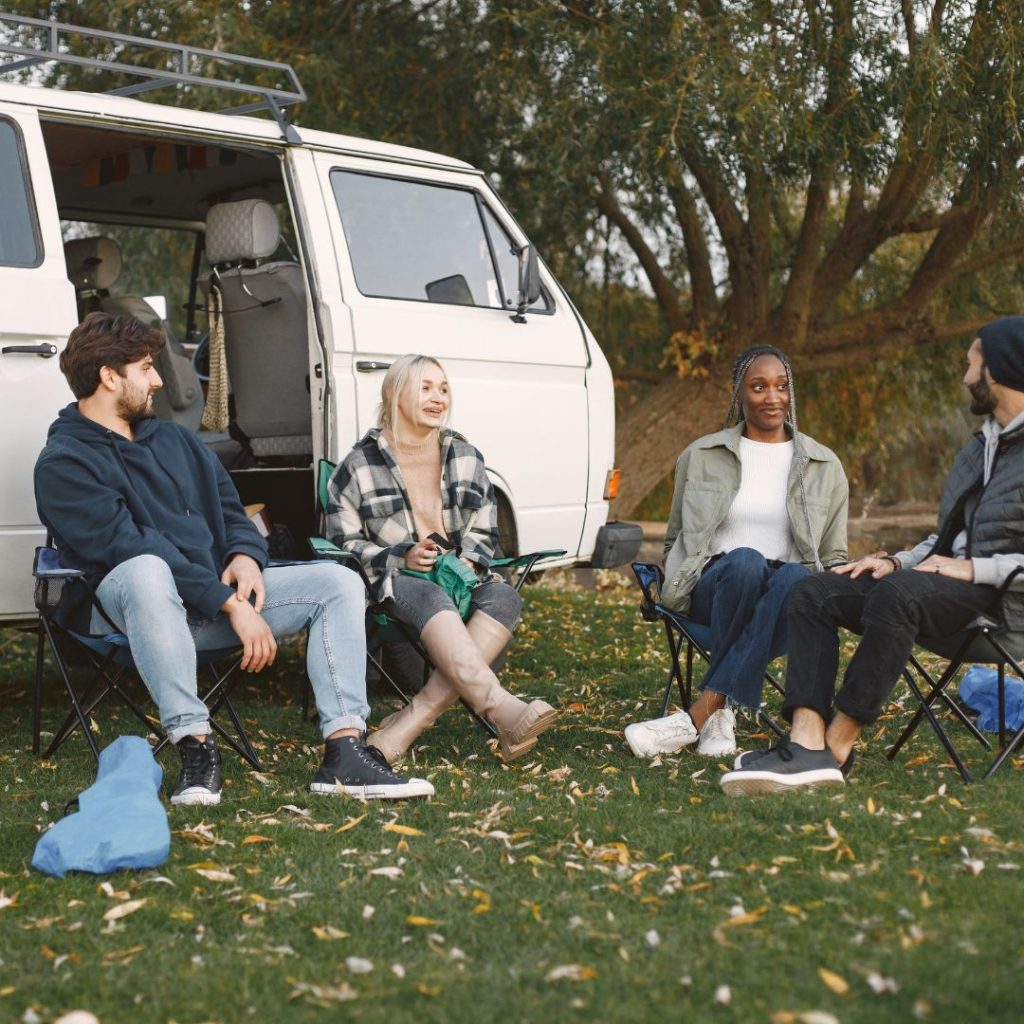 A group of people sitting in Helinox chairs in front of a camper van.