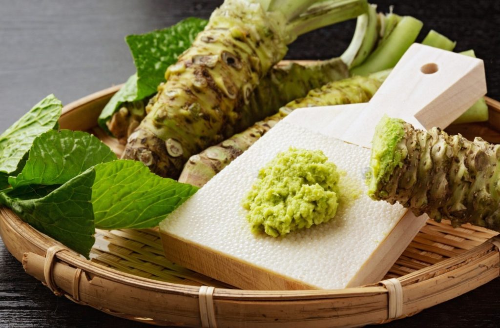 Japanese taro leaves, wasabi and green wasabi sauce on a wooden cutting board.