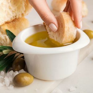 A piece of bread is dipped in a ramekin of olive oil.