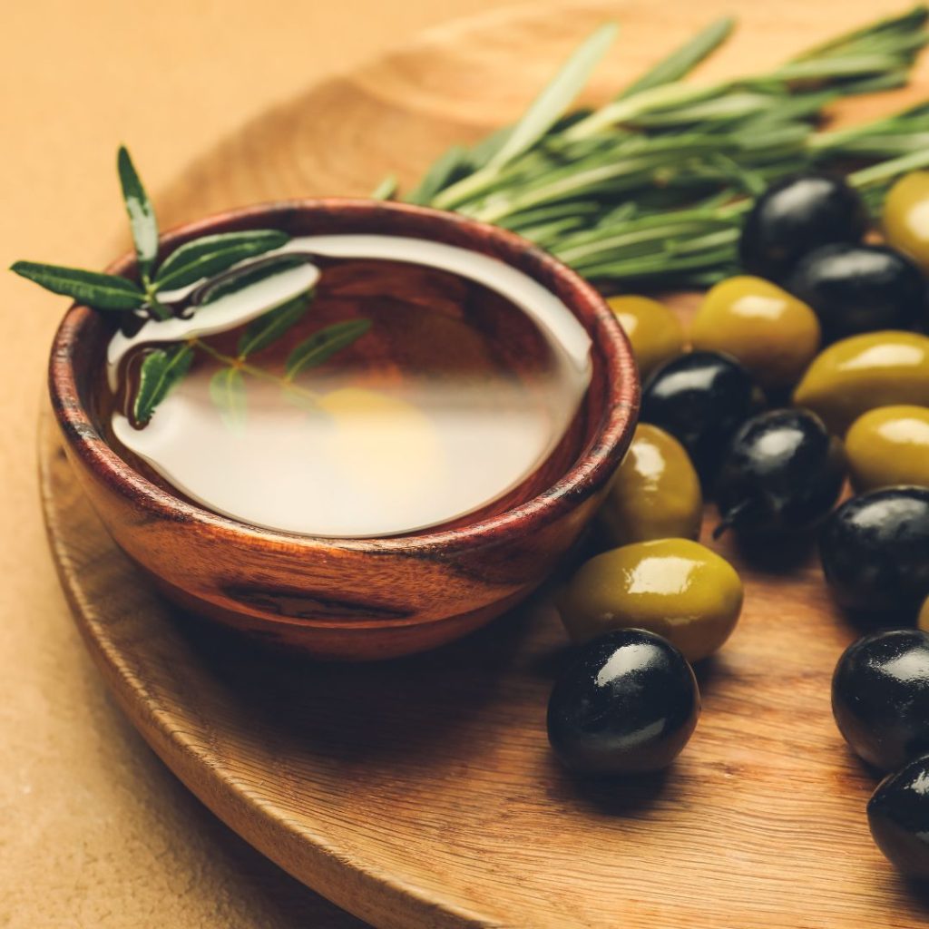 A small extra virgin olive oil bowl rests on a wooden tray with fresh olives.