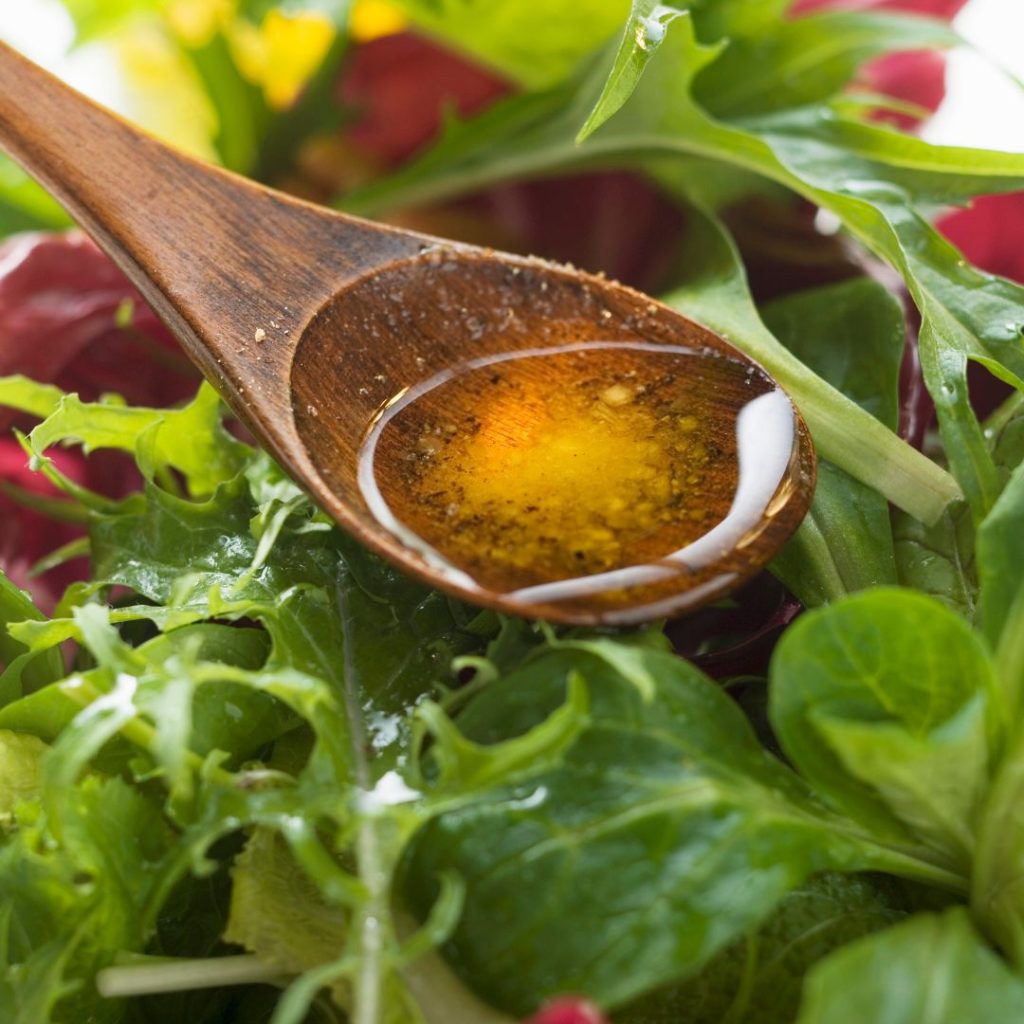 Extra virgin olive oil gets poured on a wooden spoon before drizzling into a salad bowl.