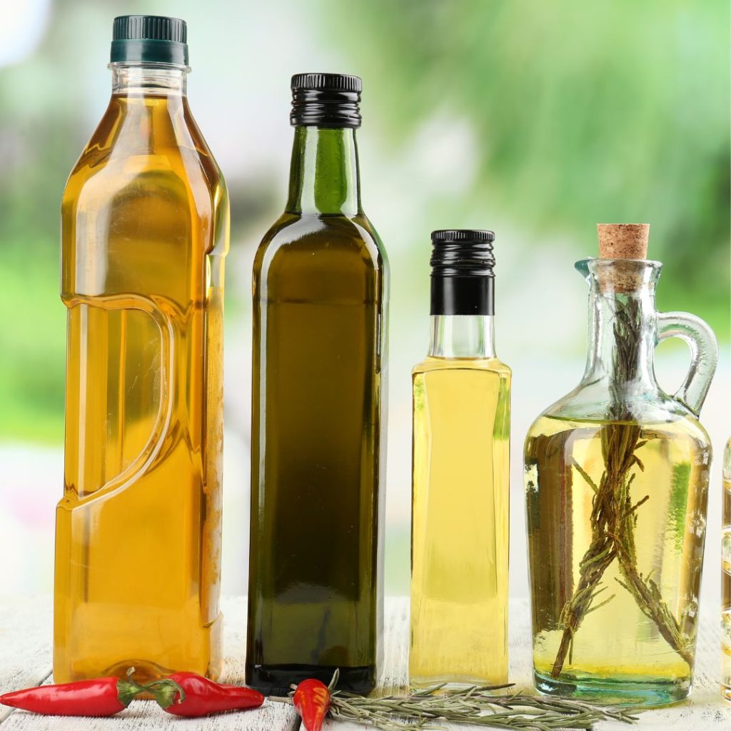 Four bottles of oils, including extra virgin olive oil and vegetable oil, rest on a wooden table with some chilis