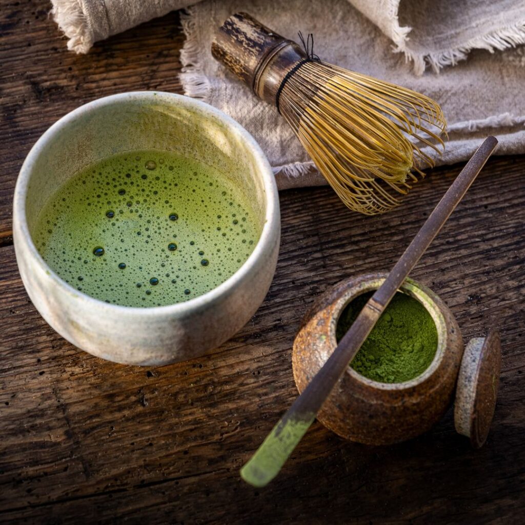 matcha in a matcha bowl with whisk and matcha powder on the side